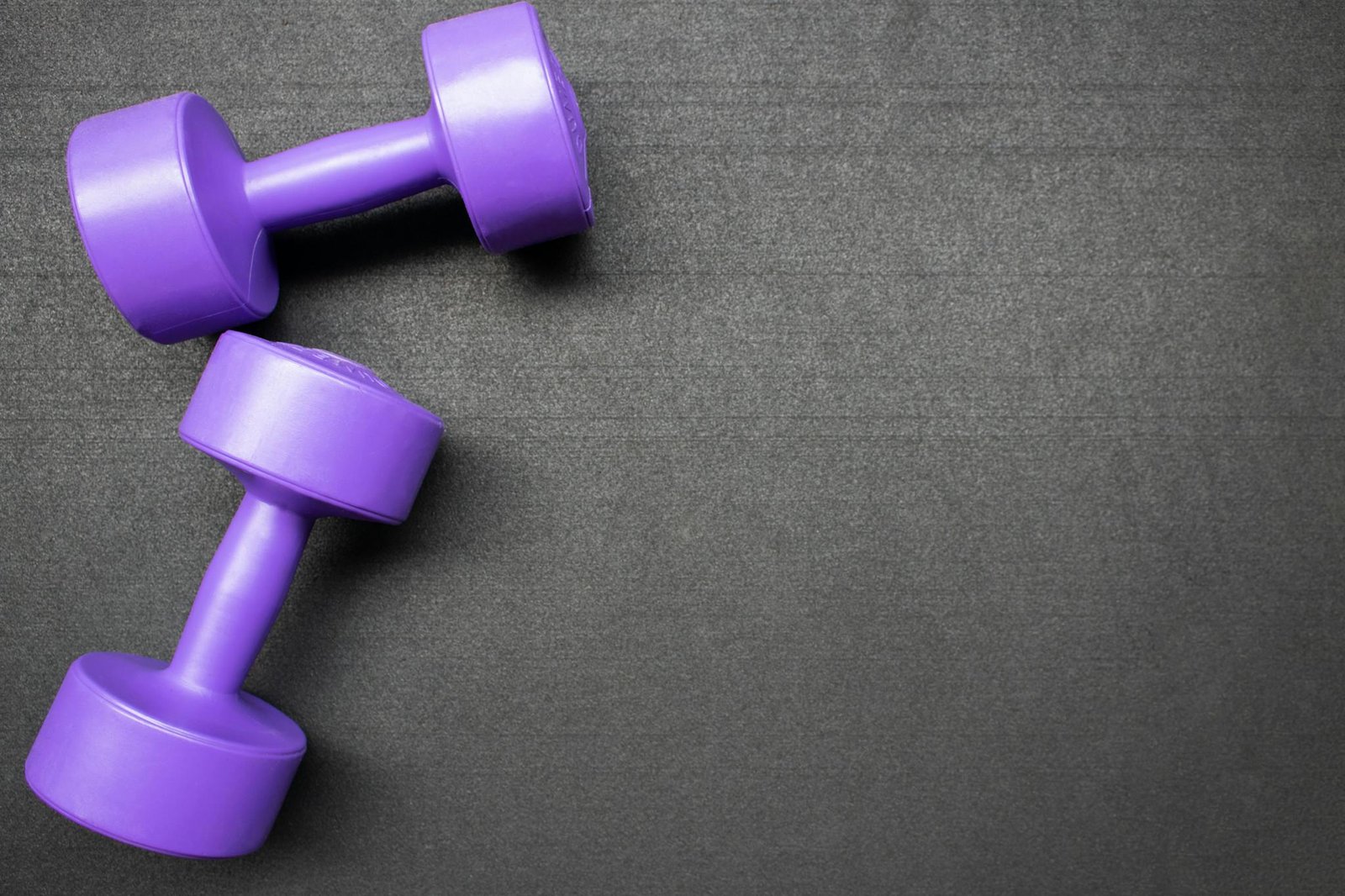 Pair of purple dumbbells on a dark gray background, perfect for fitness themes.